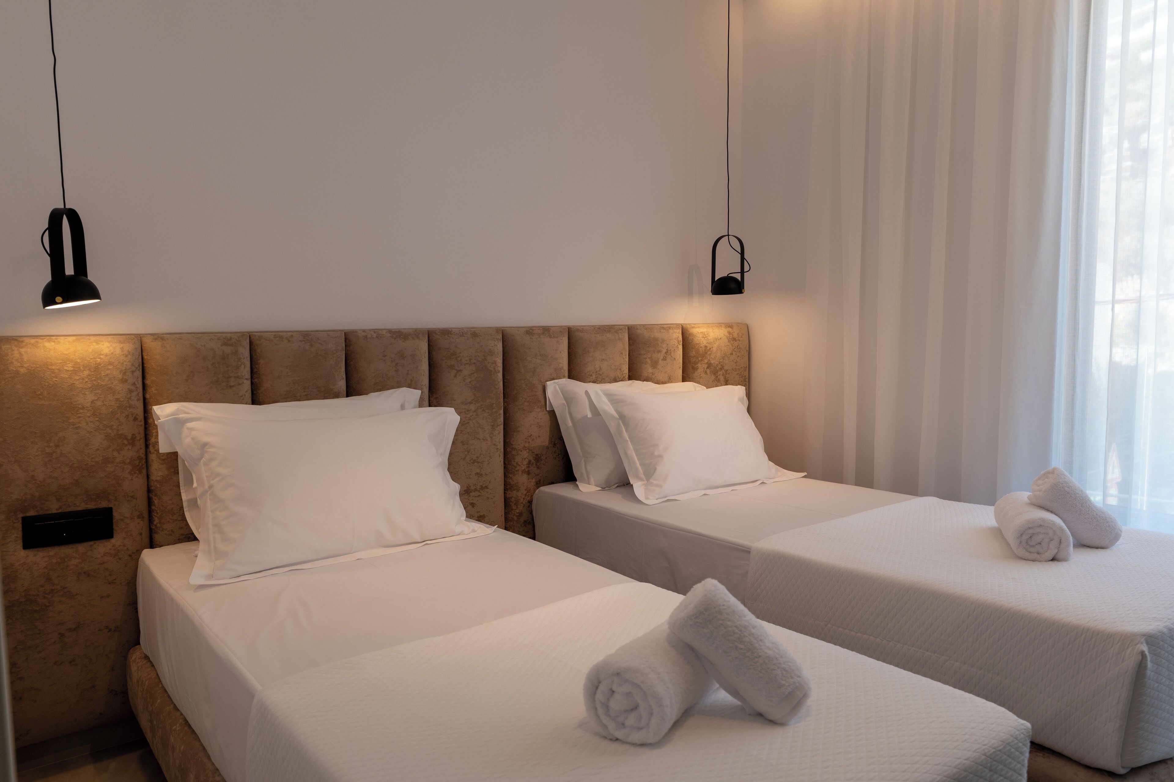 Dos camas individuales con sábanas y almohadas blancas, un cabecero y una mesita de noche.
