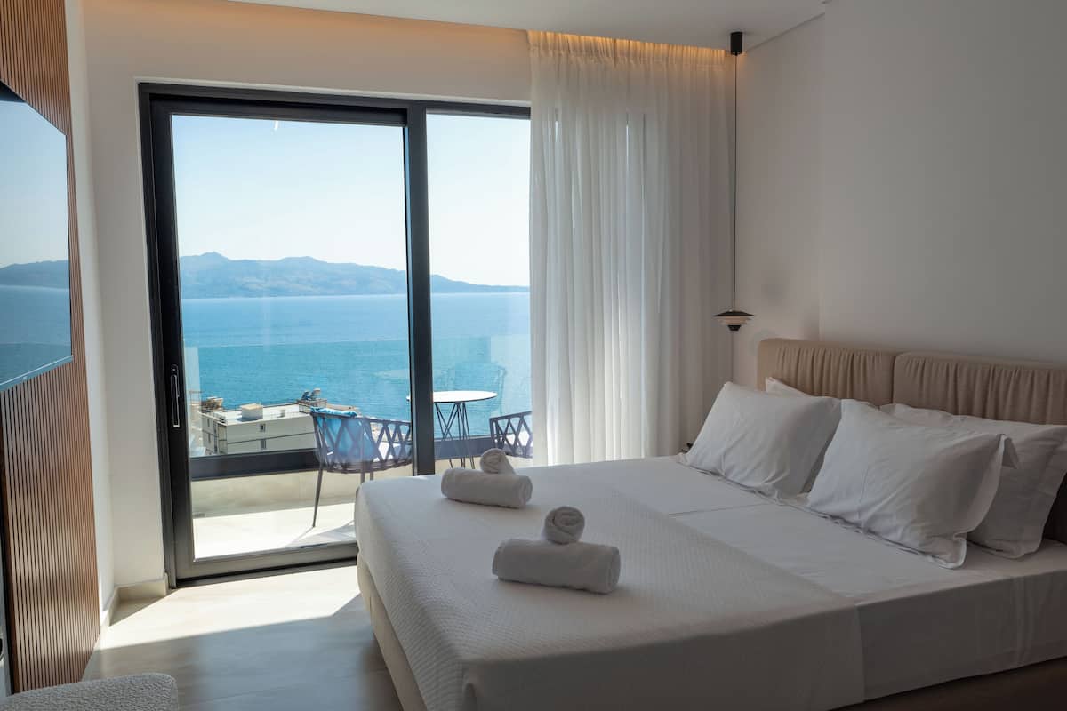 A hotel room with a large bed, a balcony with a table and chairs, and a view of the sea.