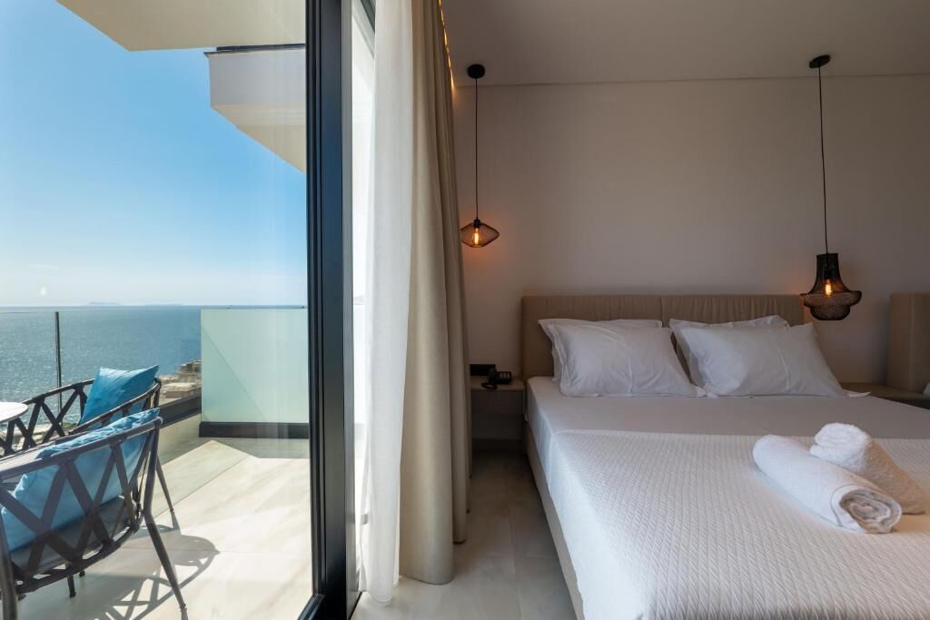 A hotel room with a bed, a nightstand, a chair, and a view of the sea.