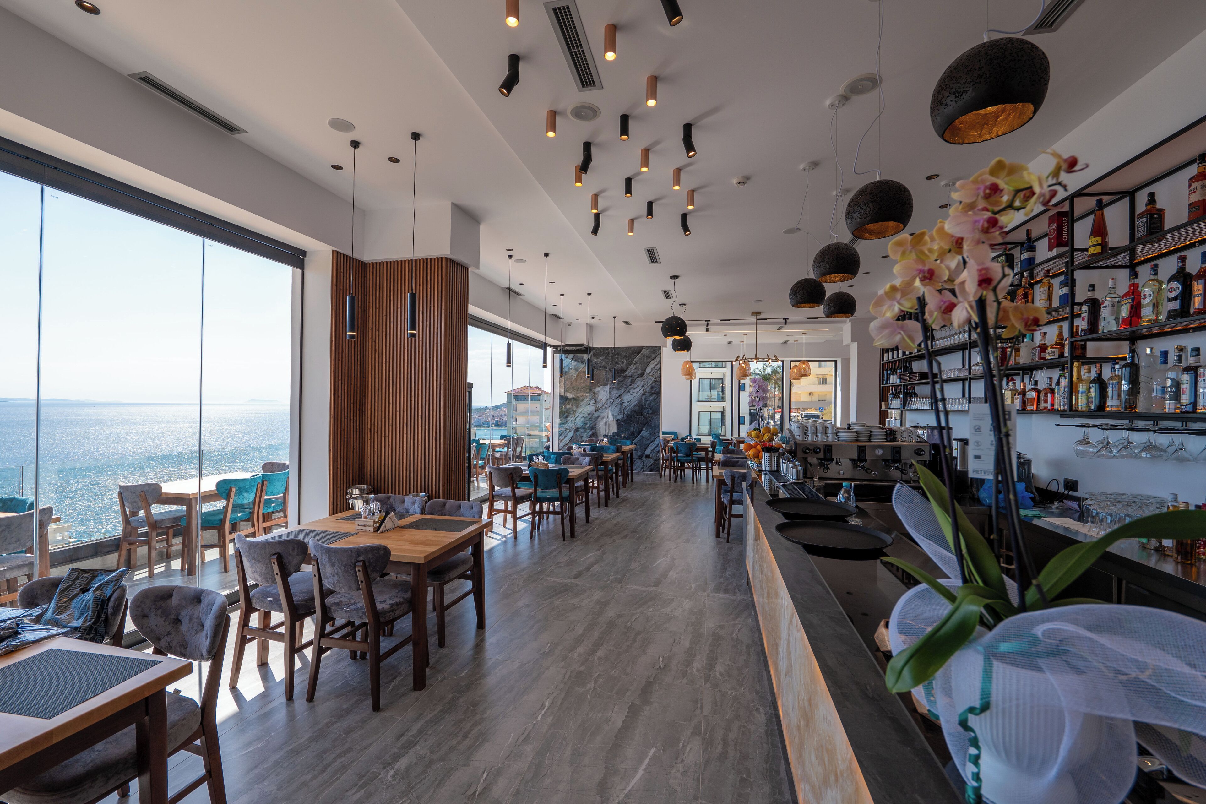 Ein modernes Restaurant mit Meerblick, Holzmöbeln und einer Bar mit Flaschenregalen.