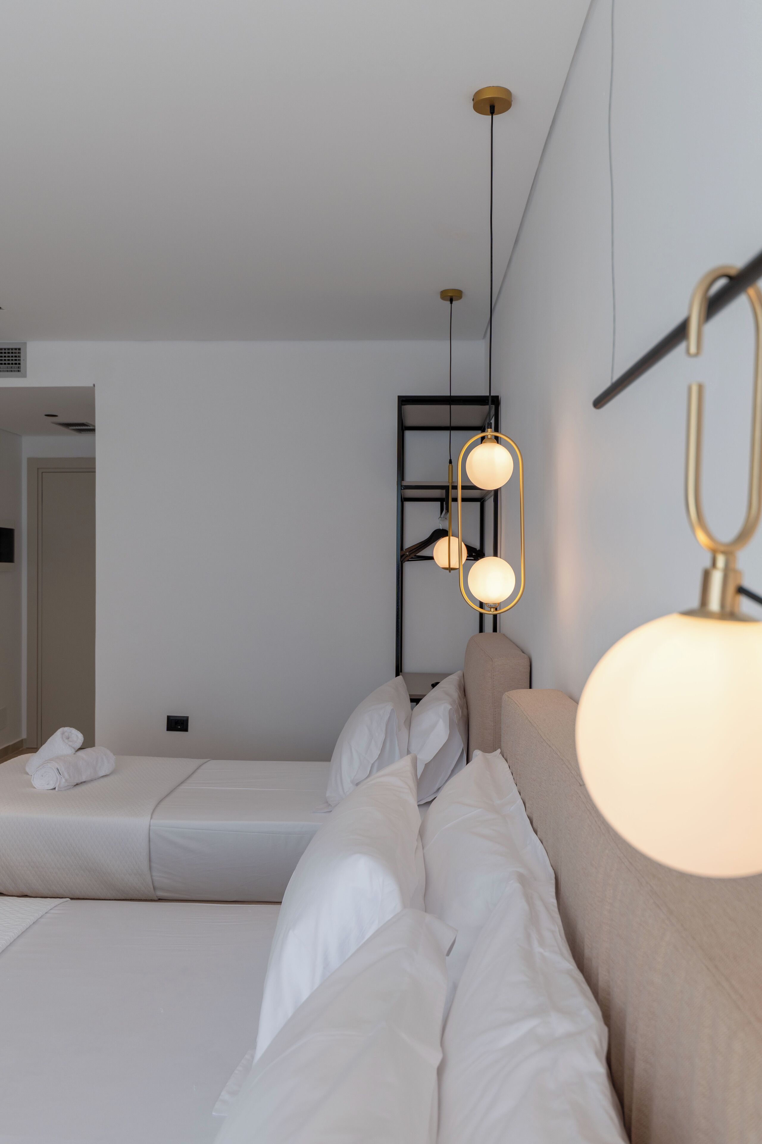 Una habitación de hotel moderna con dos camas, una mesita de noche y una lámpara colgante.