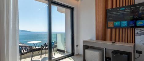 A modern hotel room with a balcony, a TV mounted on the wall, and a small desk area.