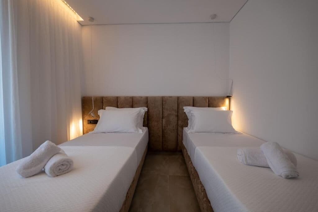 Una habitación de hotel con dos camas individuales, cada una con cubrecama y almohadas blancas, y cabeceros de madera.