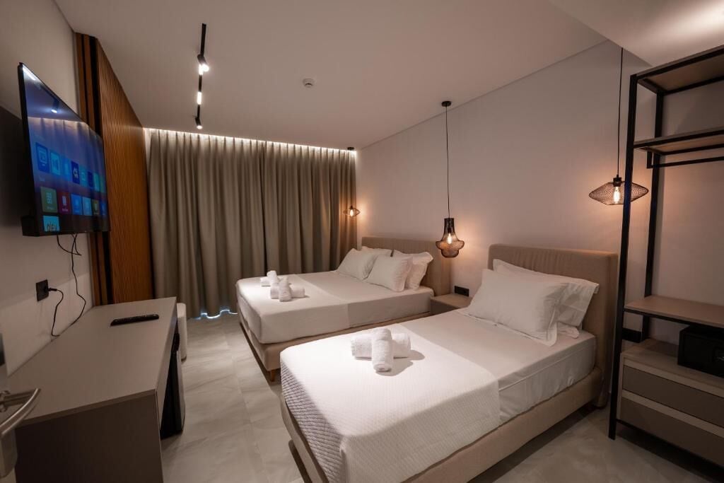 A modern hotel room with two beds, a desk, a TV, and a large window with curtains.