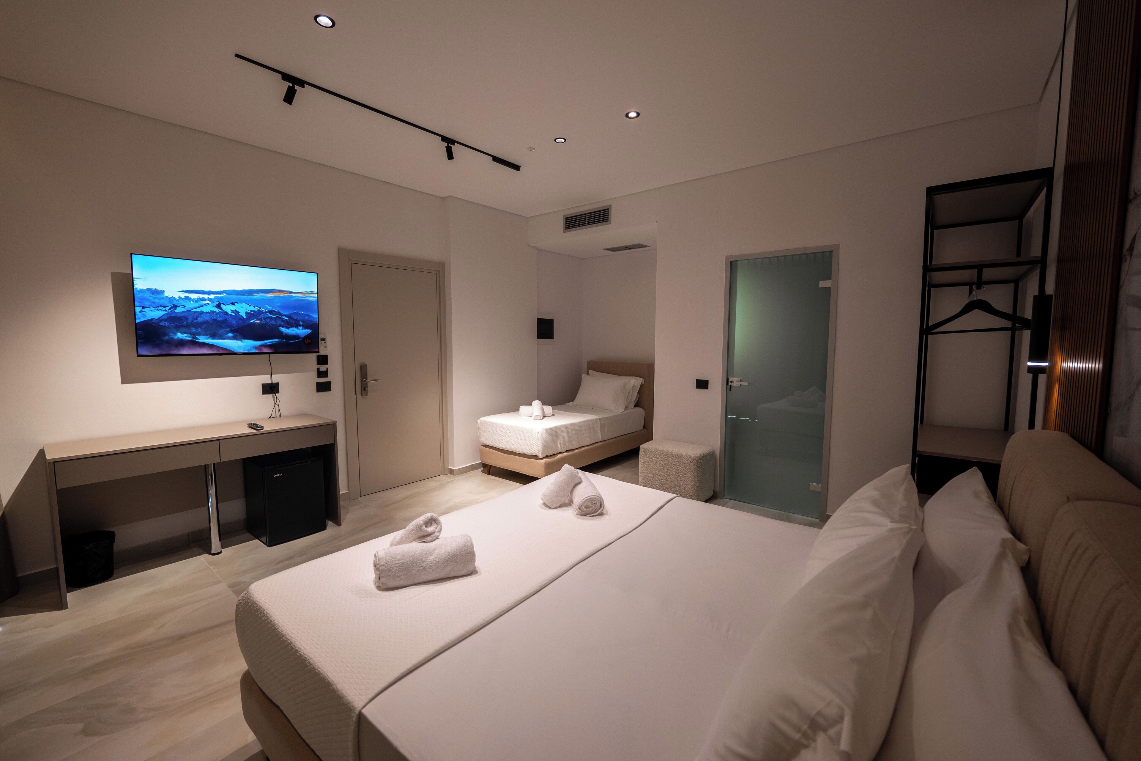 A modern hotel room with a large bed, a desk, a television, and a walk-in closet.