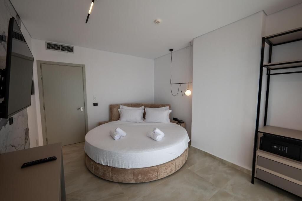 A modern hotel room with a round bed, a TV mounted on the wall, a bedside table, and a built-in shelf.