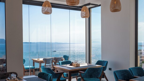 A modern dining area with large windows, wooden tables, and blue upholstered chairs. - Litan Hotel (Sarandë)