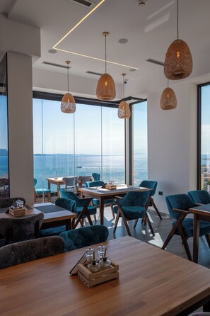 A modern dining area with large windows, wooden tables, and blue upholstered chairs. - Litan Hotel (Sarandë)