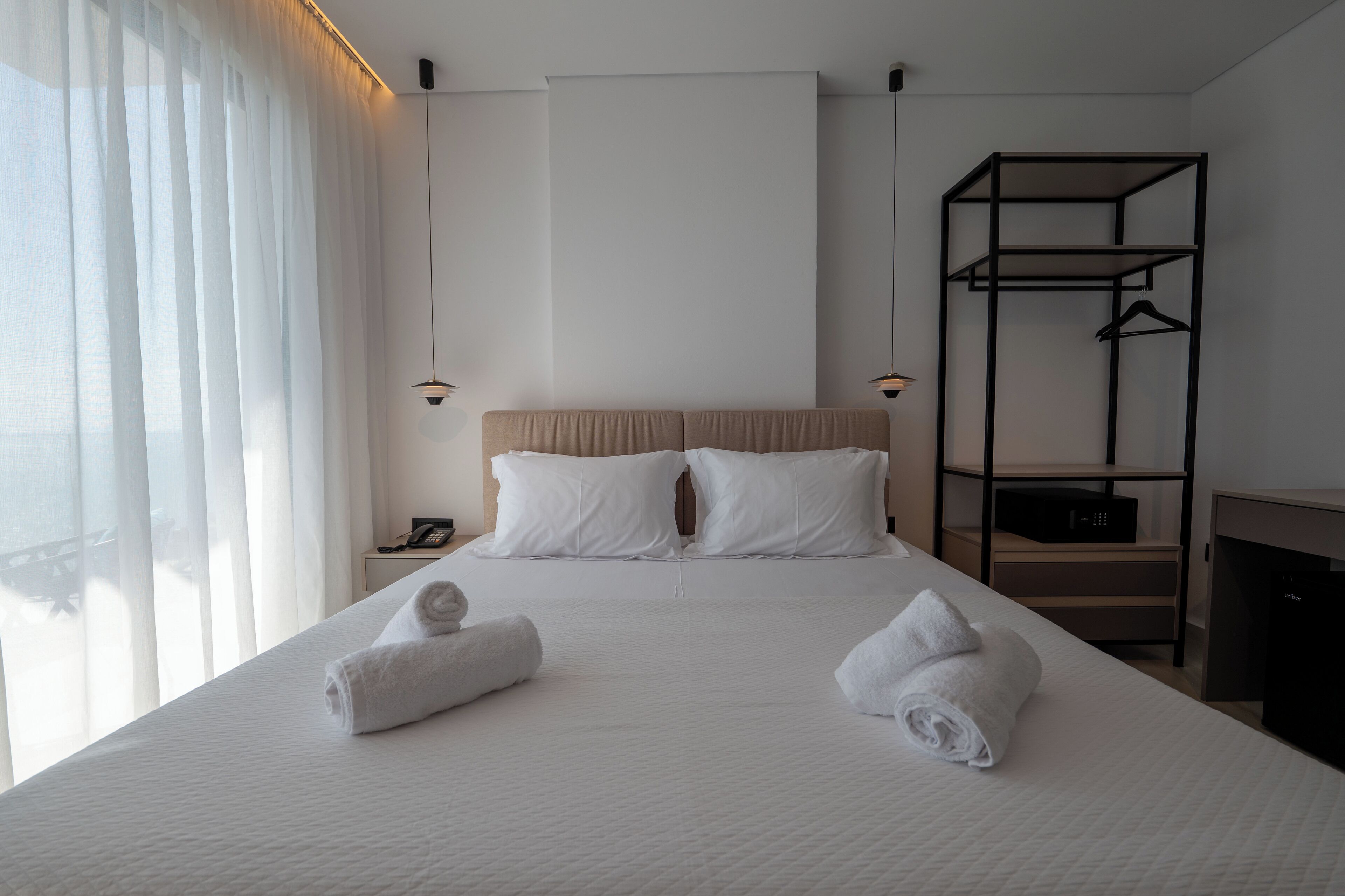 A neatly made bed with two towels, a bedside table with a phone, and a black hanging rack.