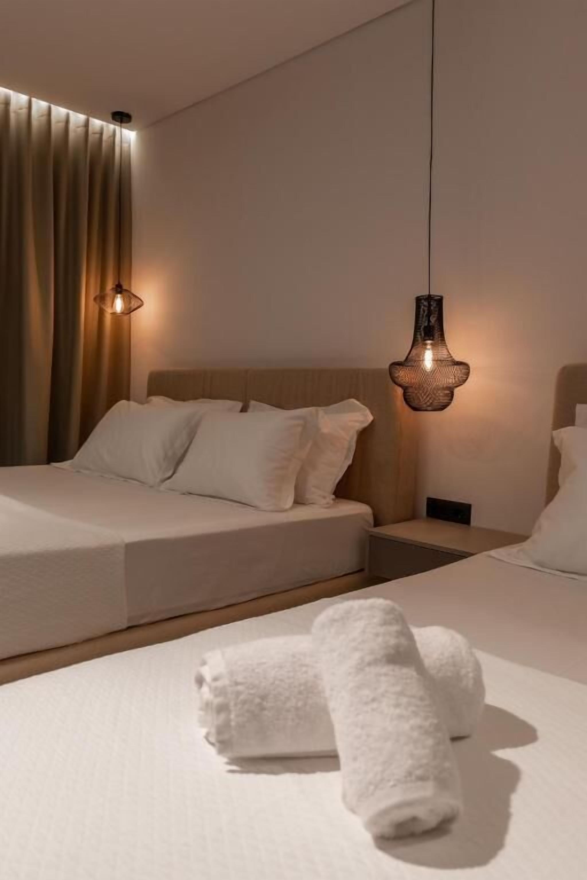 Une chambre d’hôtel moderne avec un grand lit, une table de chevet et un luminaire suspendu.