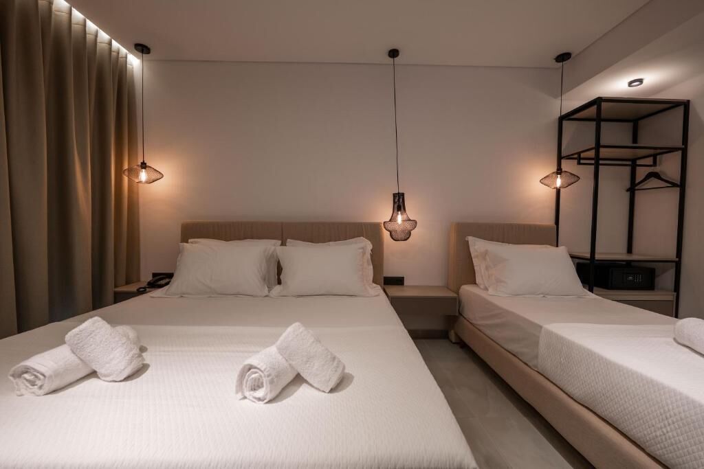 A hotel room with two beds, a wardrobe, and a nightstand with a lamp.