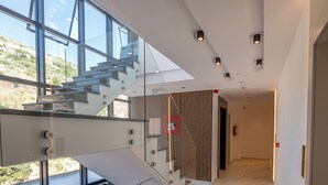 A modern interior with a glass staircase, marble flooring, and a view through large windows. - Litan Hotel (Sarandë)