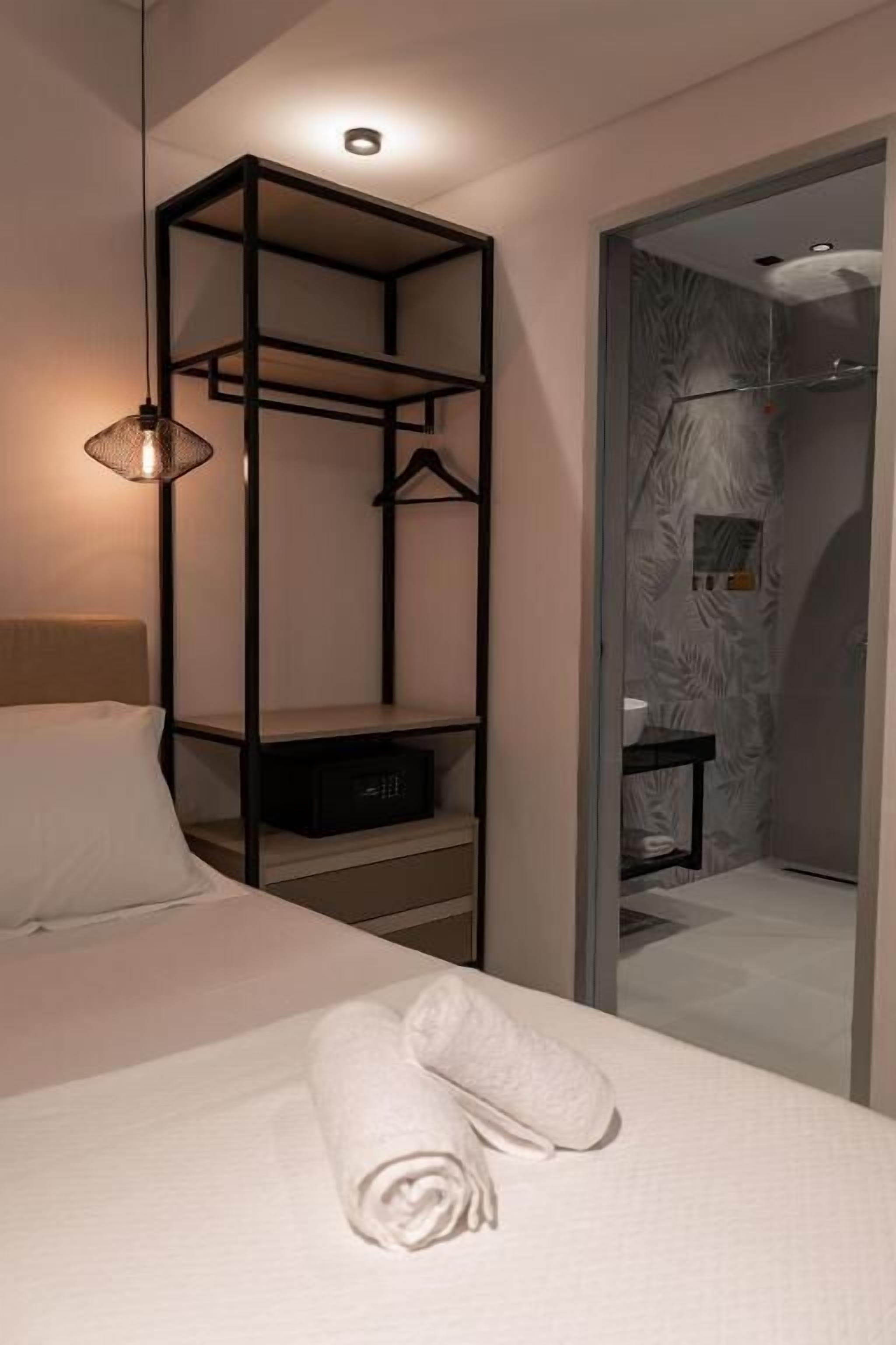 A modern hotel room with a neatly made bed, a hanging light fixture, a built-in wardrobe, and a shower area visible through a glass door.