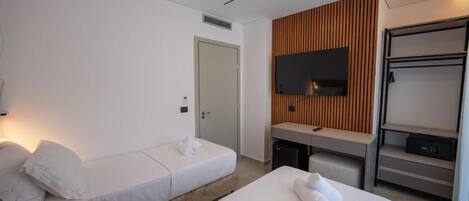 A hotel room with two single beds, a TV mounted on a wooden panel wall, a desk with a chair, and a wardrobe.