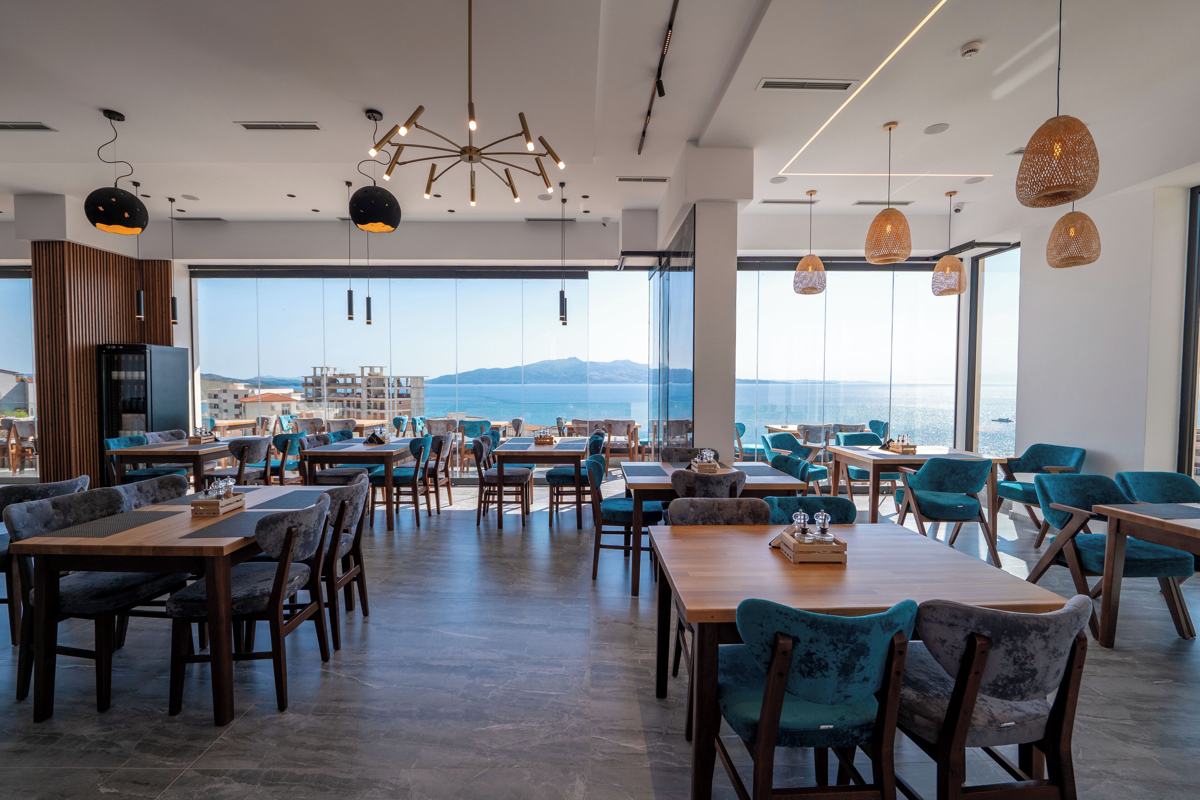 A spacious dining area with high tables and chairs, large windows offering a view of the sea, and modern pendant lighting.