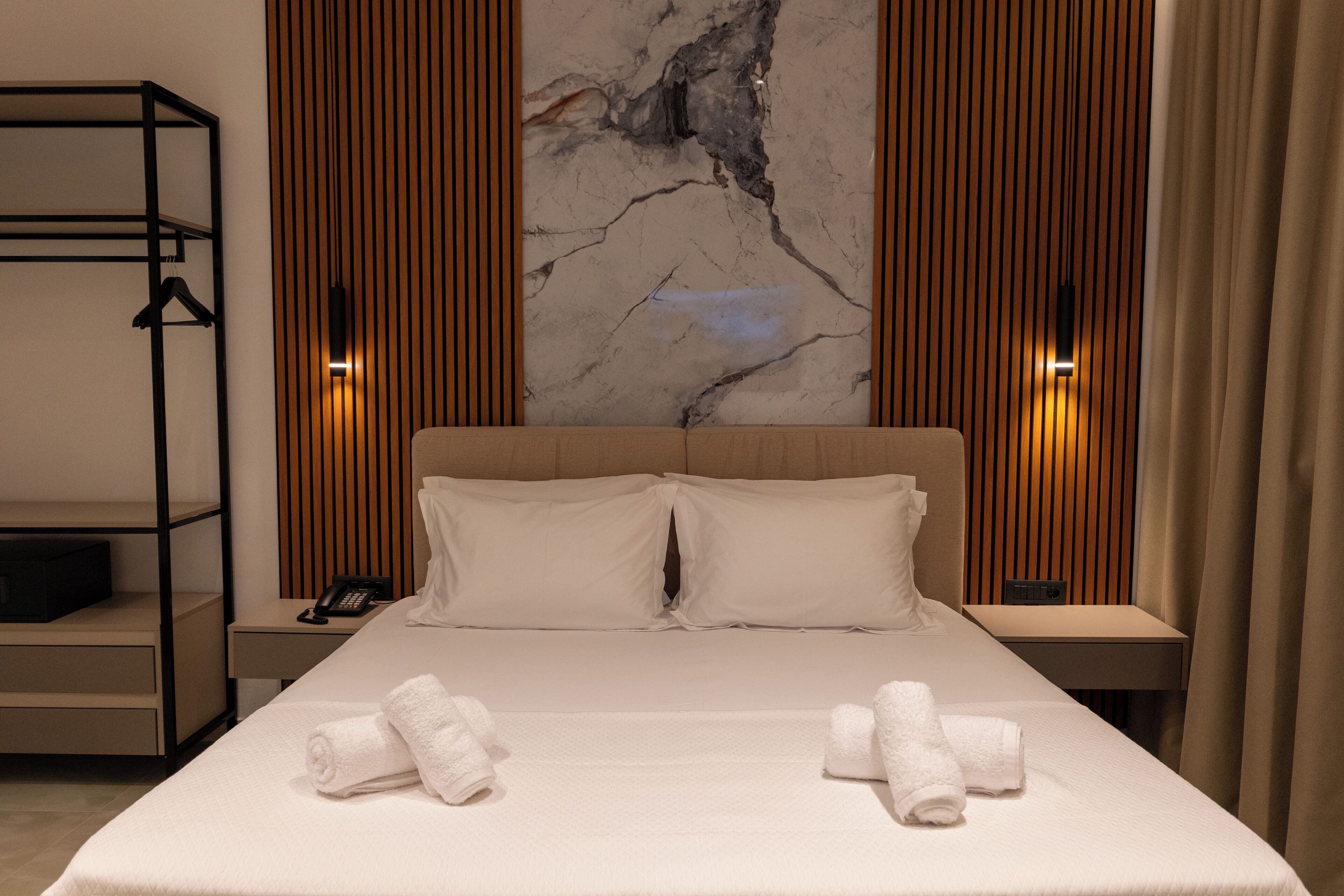Habitación de hotel con una cama grande, dos mesitas de noche, un teléfono en la pared y un armario ropero.
