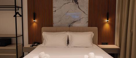 Habitación de hotel con una cama grande, dos mesitas de noche, un teléfono en la pared y un armario ropero.
