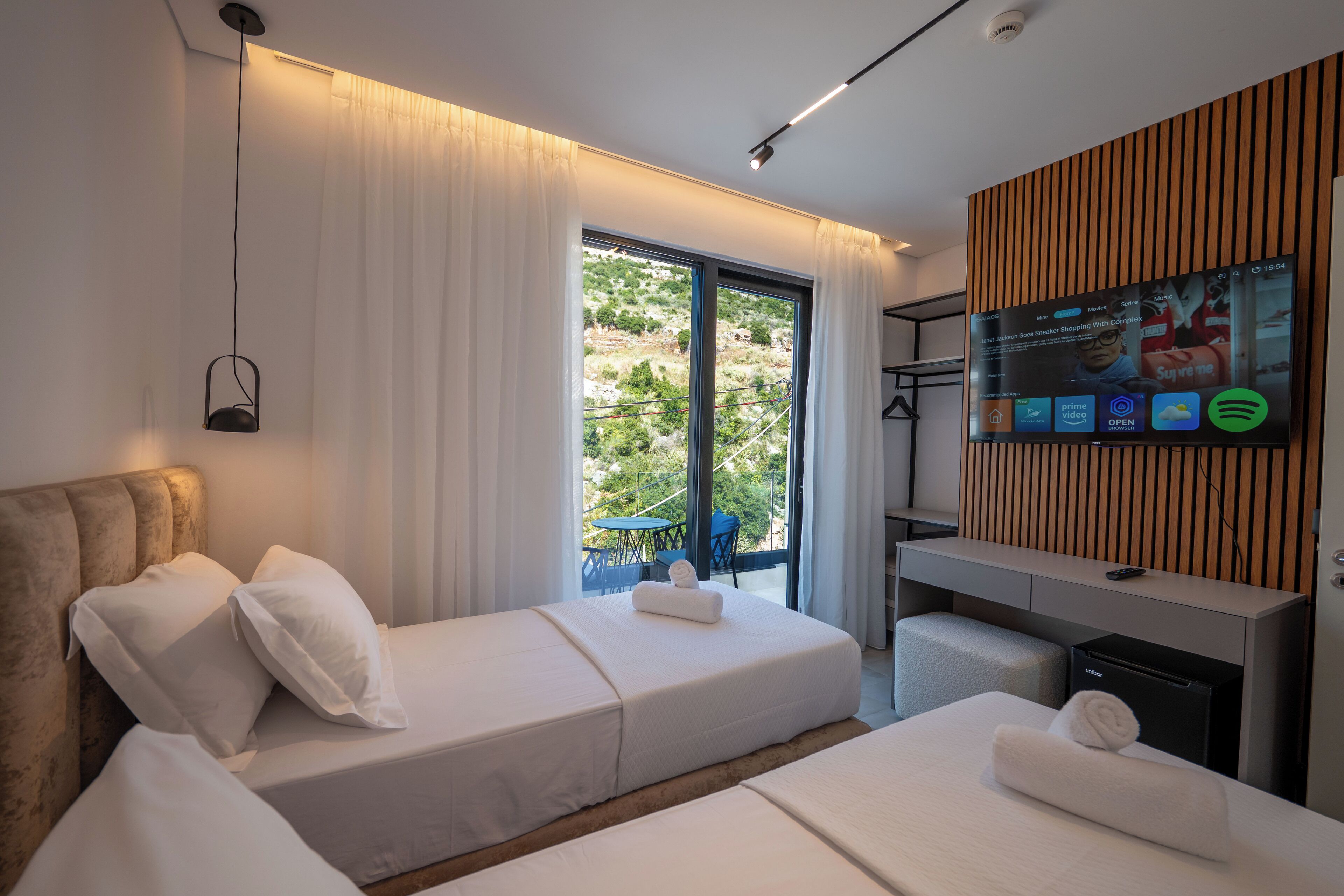A modern hotel room with a bed, a desk, and a TV displaying various apps.