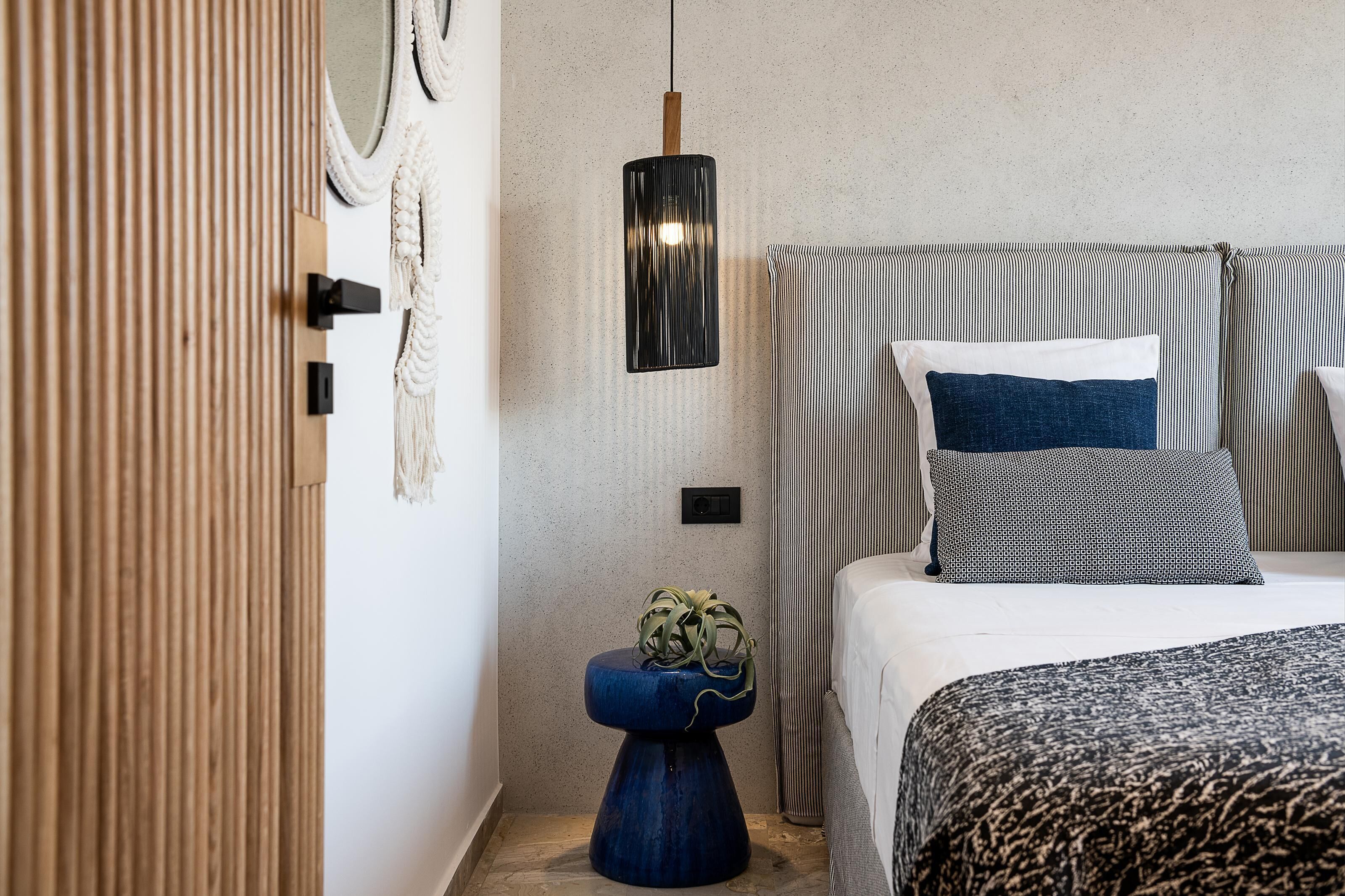 A bedroom with a bed, a bedside table with a plant, a wall-mounted light, and a striped curtain.