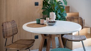 A round table with a white top, surrounded by wicker chairs, a bowl of fruit, and a coffee maker.