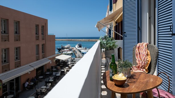 A balcony with a table, chairs, and a view of the sea and boats.