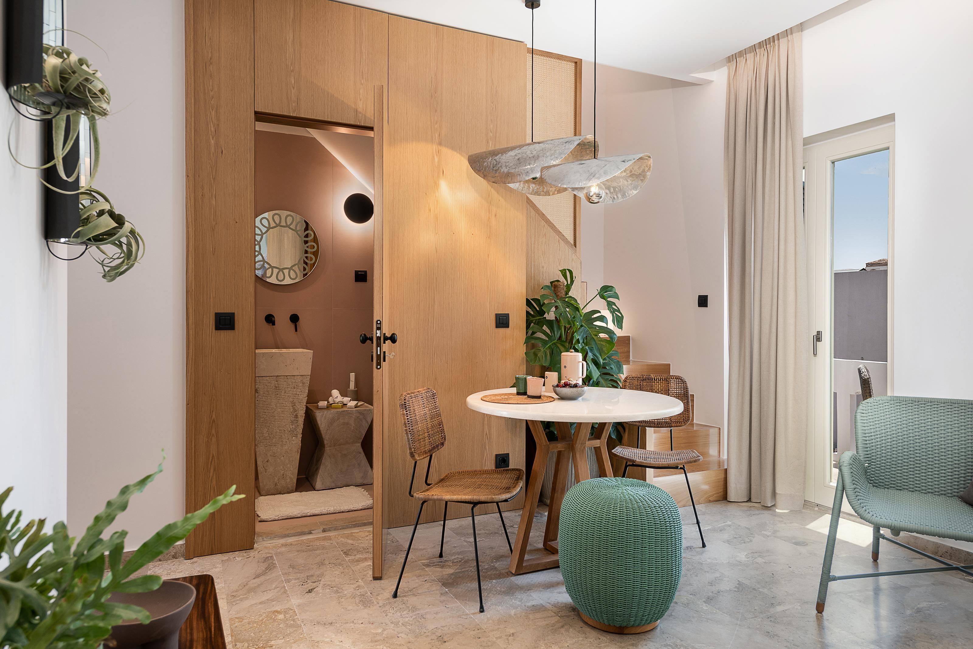 A modern dining area with a round table, wicker chairs, and a hanging light fixture.