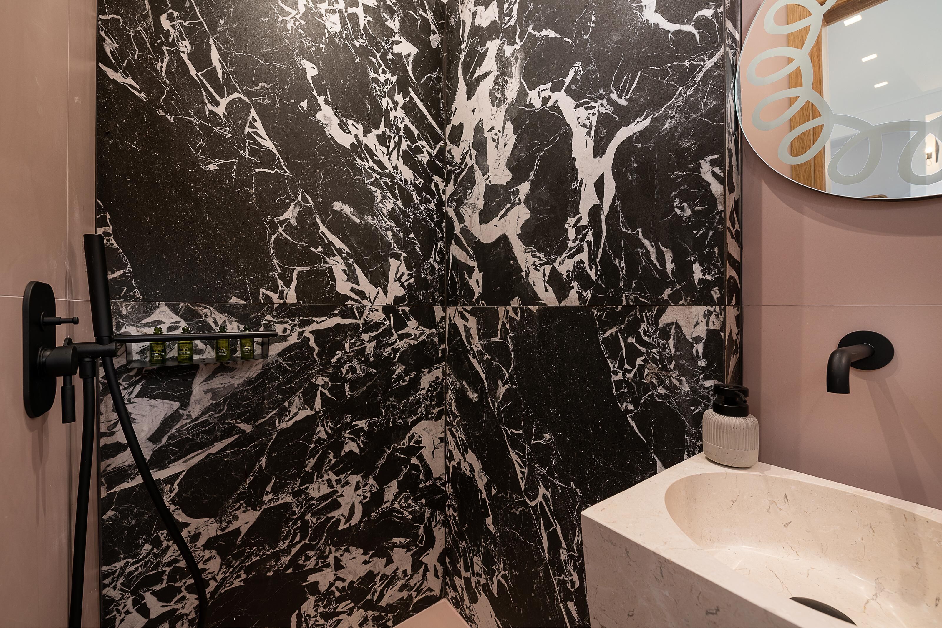 Un baño con pared de mármol blanco y negro, un lavamanos blanco y un espejo con marco decorativo.