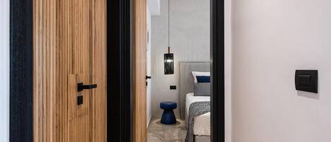 Un couloir étroit mène à une chambre qui contient un lit, une table de chevet et un luminaire suspendu.