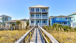 A multi-story beachfront building with a wooden boardwalk leading to it, surrounded by vegetation. - ☀️Ocean Oasis- Oceanfront w/Stunning Views-Pet Friendly☀️ (Carolina Beach)