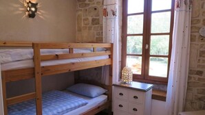 Ein Schlafzimmer mit Etagenbetten, einer Steinsandsteinwand, einem Fenster mit Vorhängen und einem Nachttisch mit Schubladen.
