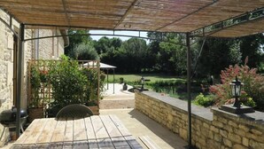 Ein überdachter Patio-Bereich mit einer Steinwand, einem Holztisch und einem Grill.