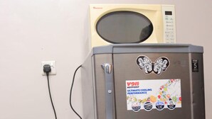 Ruostumattomasta teräksestä valmistettu jääkaappi, jossa on Von Hotpoint -tarrat, mikroaaltouuni sen päällä ja virtajohto, joka on kytketty pistorasiaan.