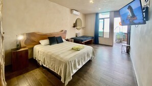 A bedroom with a large bed, a desk, a TV, and a balcony with plants. - Hotel downtown private room with pool. (Cancún)