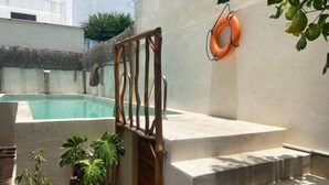 A pool area with steps leading to a door, surrounded by potted plants and a lifebuoy on the wall. - Hotel downtown private room with pool. (Cancún)