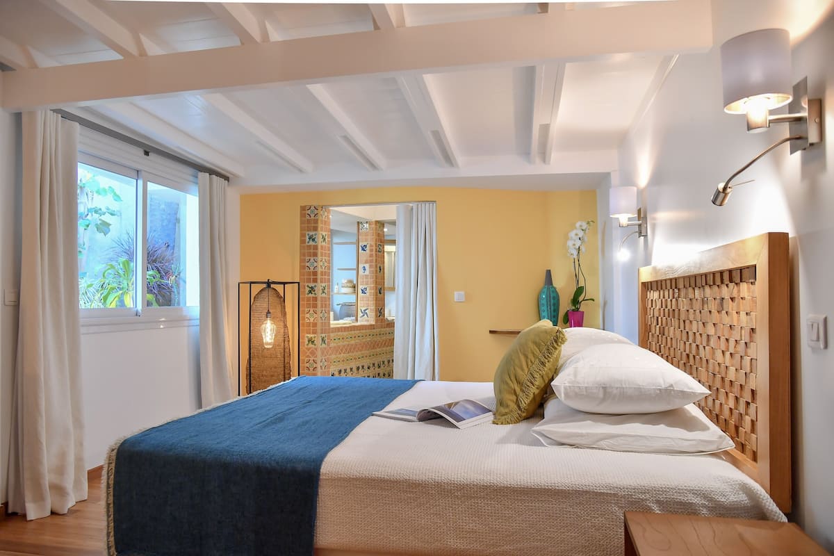 Een slaapkamer met een bed, een houten hoofdbord, een nachtkastje en een raam met gordijnen.