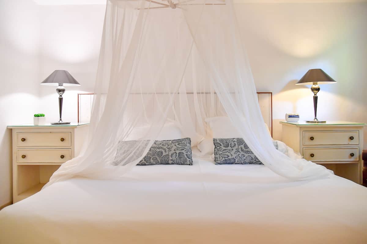 Een bed met hemel, twee nachtkastjes met lampen, en gestreepte kussens.