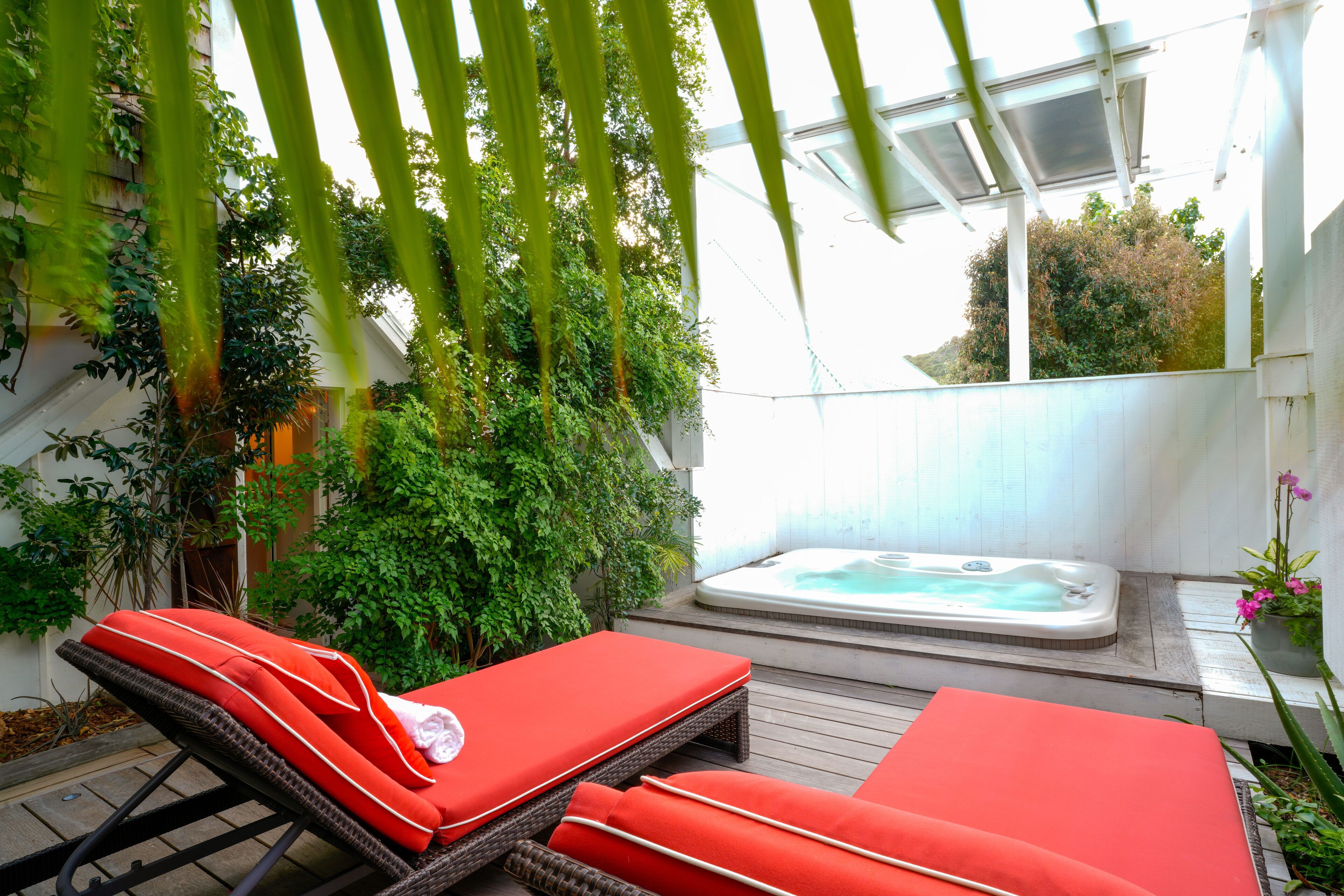 Un espacio al aire libre iluminado por el sol con dos sillones rojos, un jacuzzi y abundante vegetación.