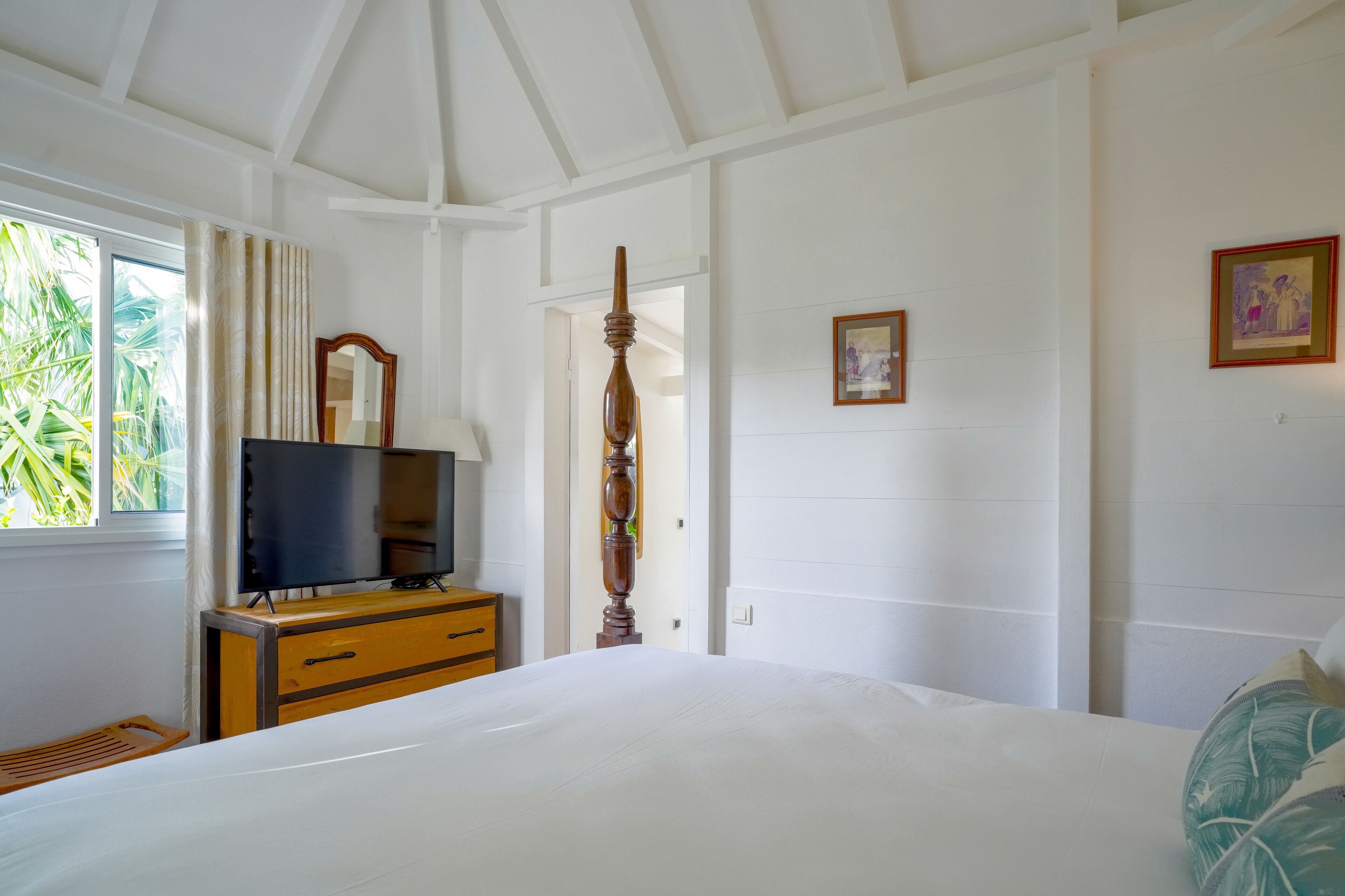 A bedroom with a bed, a wooden dresser, a television, and a door leading to another room.