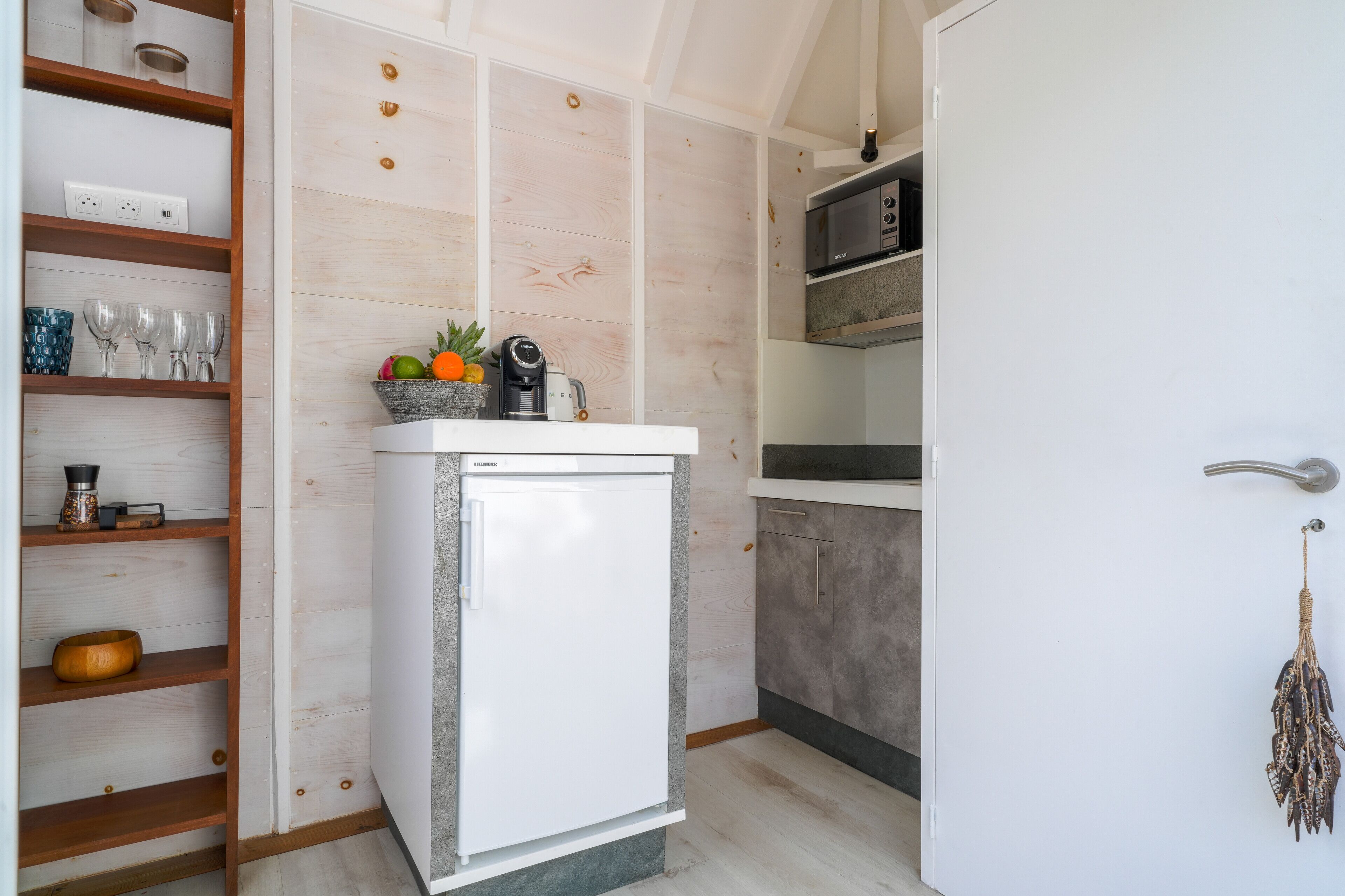 A compact kitchen with a built-in refrigerator, wooden shelves, and a microwave.
