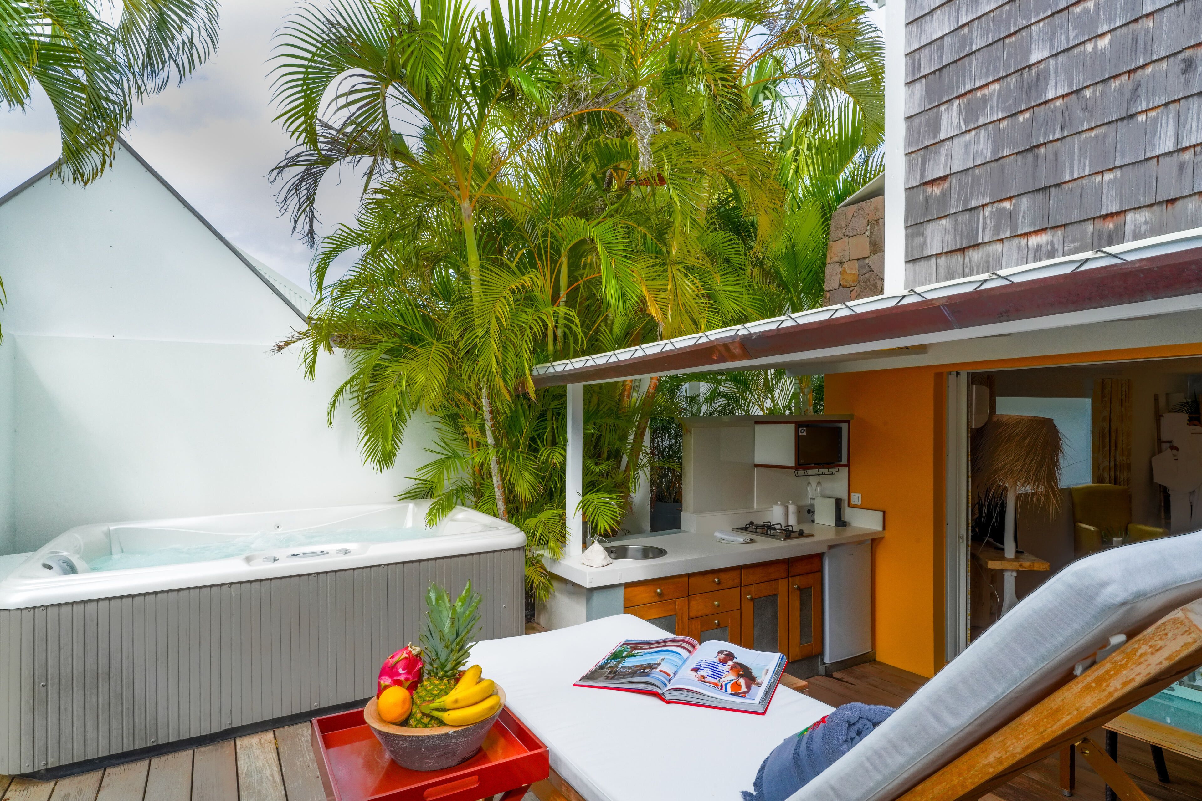 A modern outdoor living area with a hot tub, a lounge chair, and a dining table with fruits.