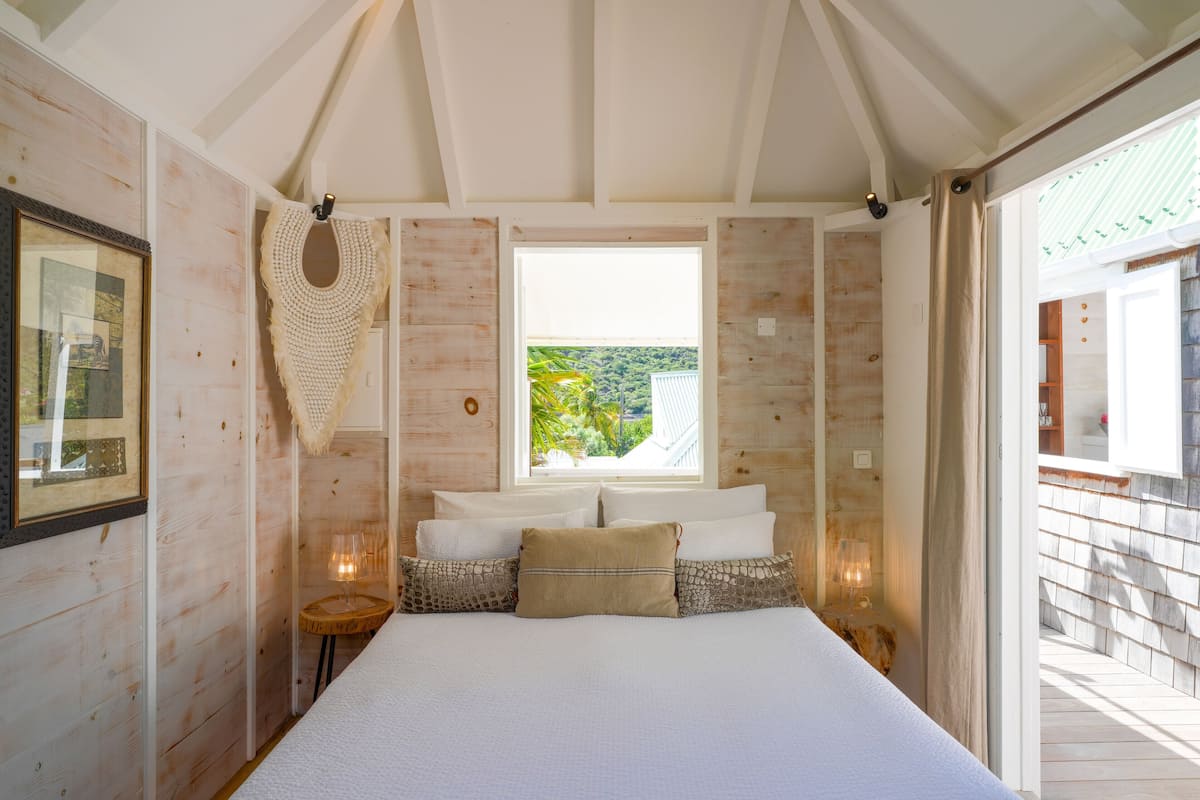 Een slaapkamer met een groot bed, een raam met uitzicht op groen, houten wanden en een lijst met een afbeelding aan de linkerkant.