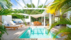 A pool area with lounge chairs and a table, surrounded by wooden decking and greenery. - La Maison Fleur de Lune (St. Barthelemy)