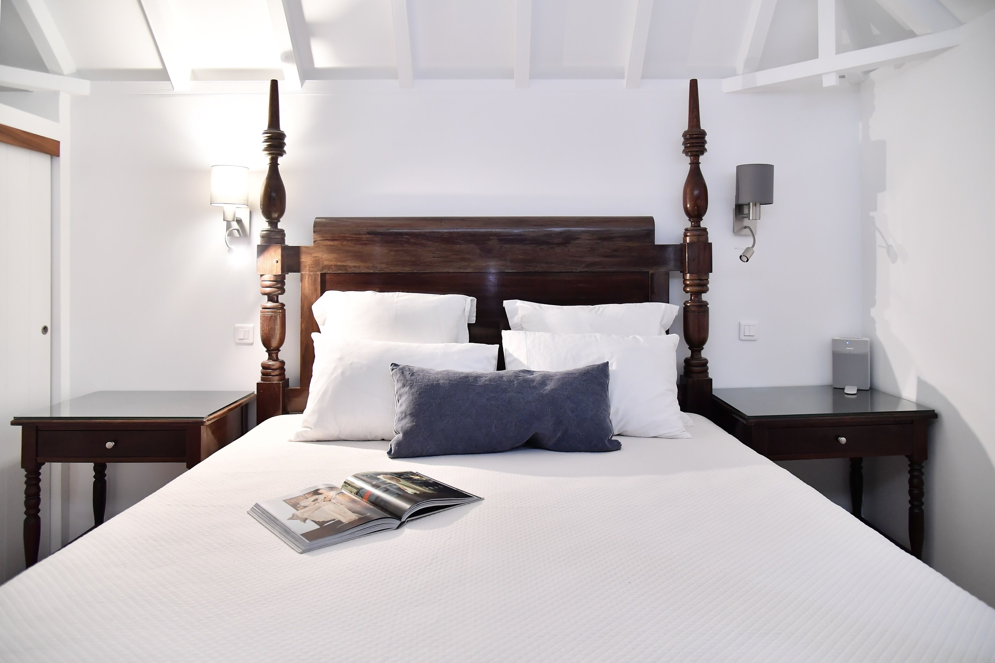 A neatly made bed with a wooden headboard, white and gray pillows, and a magazine on the bed.