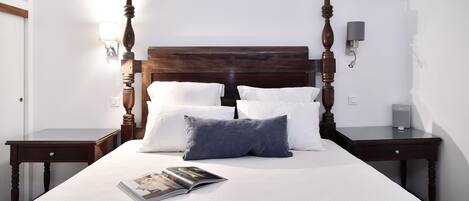 A neatly made bed with a wooden headboard, white and gray pillows, and a magazine on the bed.