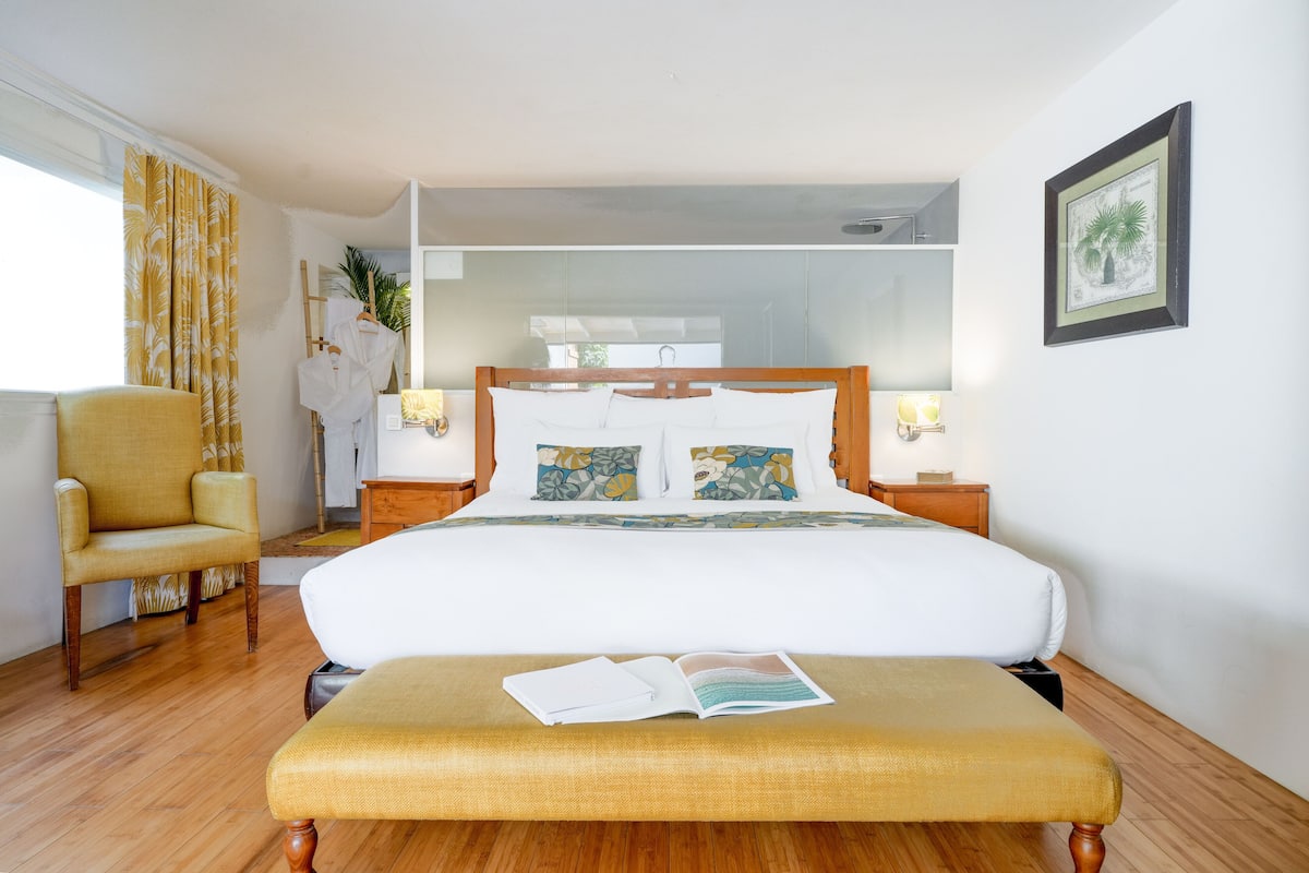 Een hotelkamer met een groot bed, een nachtkastje, een stoel en een raam met gordijnen.