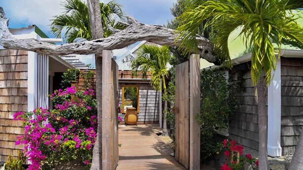 A wooden pathway leading to a house with a stone wall and a large pot in the center. - La Maison Fleur de Lune (St. Barthelemy)