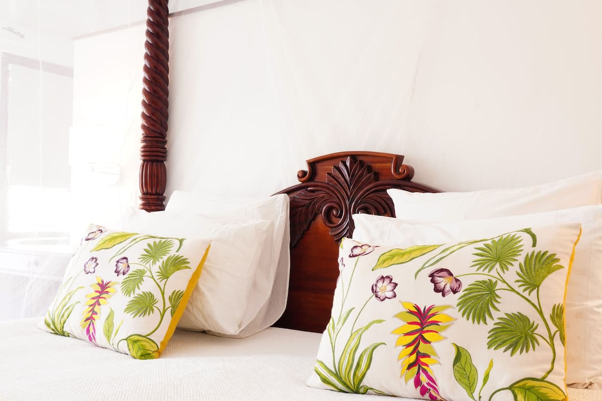 Een bed met hemel, bloemenkussens en een houten hoofdbord.