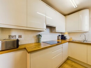 A modern kitchen with white cabinets, a wooden countertop, a Bosch toaster, and a sink. - Cosy Covent Garden Apartment (London)