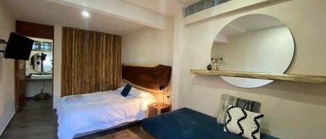 Un dormitorio con cama, mesita de noche y un espejo grande en la pared.