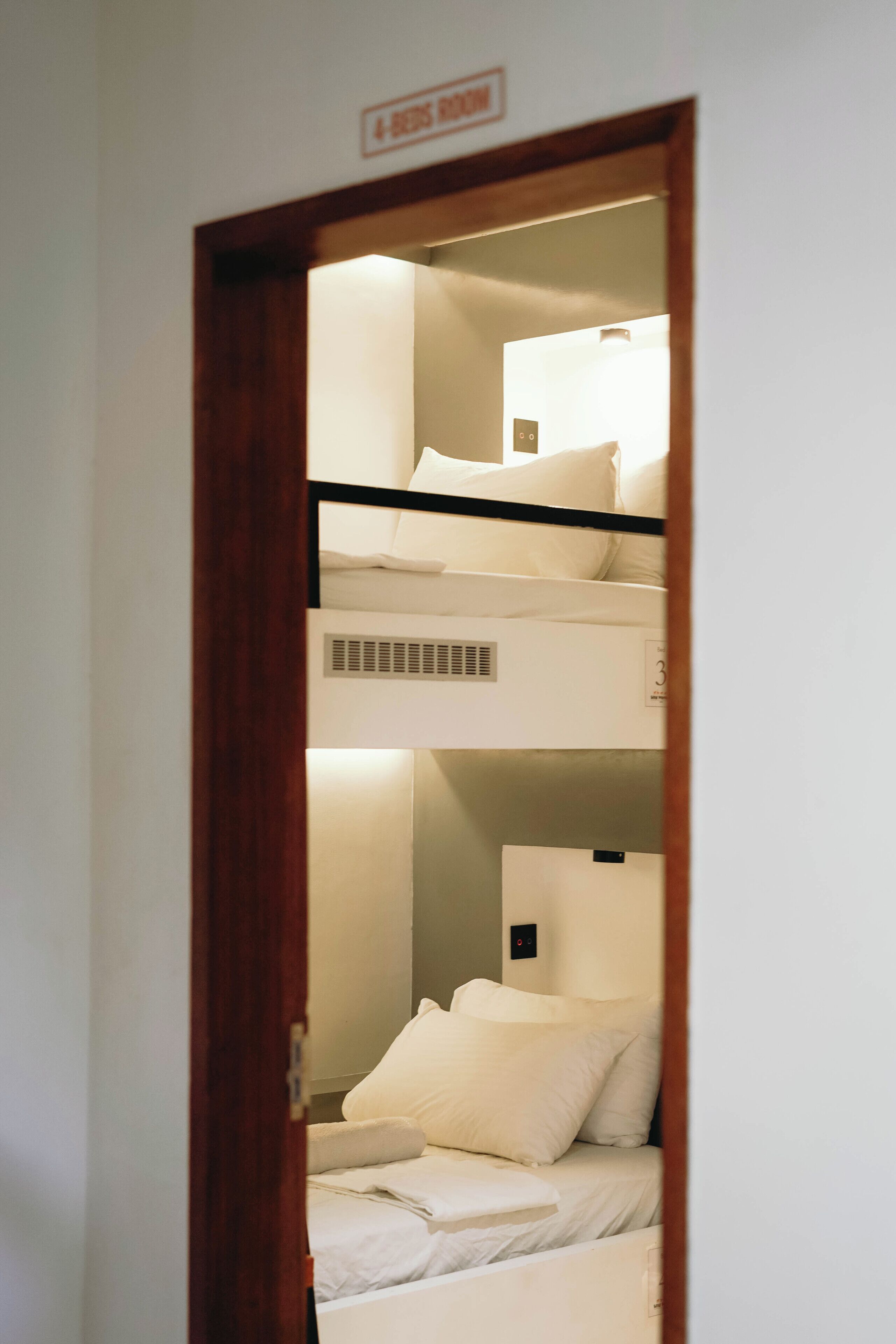 Habitación con una cama individual y una litera, ambas con ropa de cama blanca. Un cartel sobre la puerta indica el número de habitación.